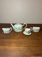 Full set: teapot, creamer, sugar bowl, teacup with saucer displayed on wood surface