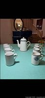 Full view of coffee pot with eight mugs on table