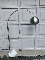 Full view of brushed steel arc floor lamp with dome shade and marble base