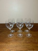 Front angled view of all six clear Mikasa Stephanie goblets on wood surface