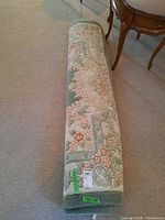 Rolled area rug showing sage green, ivory and blush floral design, full length view