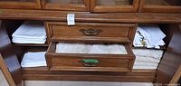 Cabinet shelves and drawers showing stacks of folded white linens including lace and embroidery
