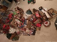 Wide view of assorted holiday decorations on floor including wreaths, boxes of ornaments, lights, nutcracker, nativity, mug