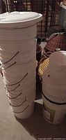 Tall stack of white 5-gallon buckets topped with an oversized lid