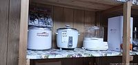Three kitchen appliances on shelf: Donvier ice cream maker, Sunbeam rice cooker, Black & Decker steamer