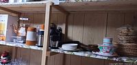 Shelf view showing teapot, thermoses, plates, bowls, wicker chargers
