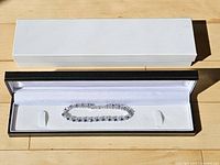 Bracelet inside open black display box with white sleeve
