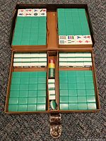 Open case showing four trays of green tiles, central area with face-up sample tiles, chips and dice