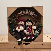 Front view of boxed holiday wreath showing snowman figures and Happy Holidays sign