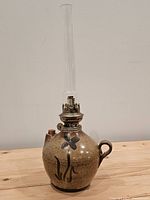 Front view showing stoneware jug lamp, brass burner and glass chimney