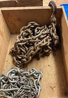 Rusted plain steel chain with forged grab hook and galvanized chain in wooden box