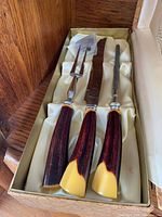 Open box displaying knife, fork and steel with phenolic handles in satin lining