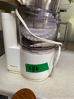 Food processor assembled with bowl, lid, cord wrapped; green label on base.