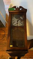 Front view of wooden wall pendulum clock showing dial, glass door and case