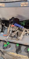 Pile of clamps on shelf including C-clamps, pistol-grip bar clamp, F-clamp, locking pliers