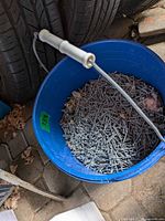 Blue plastic bucket partially filled with galvanized nails, handle visible