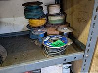 Stack of partial spools with green, yellow, white, blue and gray insulated wire on metal shelf