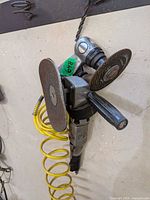 Inline and pistol-grip pneumatic angle grinders hanging with worn discs and yellow air hose