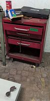 Front view of red steel rolling tool chest showing three drawers, open lower shelf and casters