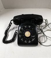 Front view of black rotary dial phone showing handset and cords