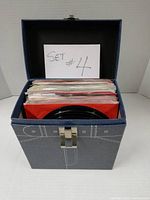 Carry case open showing stack of 45 RPM records, note 'Set #4' sign