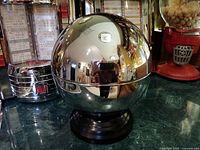 Chrome bowling ball liqueur dispenser on black base, reflective surface