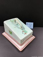 Oblique view of covered cheese dish showing floral decoration and base