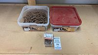 Two plastic tubs and one clamshell pack of brown deck screws on workbench