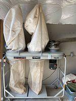 Front view of Delta dust collector showing dual upper filter bags, dual lower collection bags, blower housing and stand