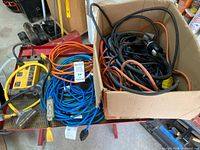 Box of assorted black and orange extension cords beside blue and orange cords on cart