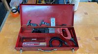 Open red case displaying Milwaukee Sawzall, blade pack, loose blades and clamps