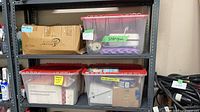 Shelving with three visible clear totes with red lids and labelled contents plus a cardboard box showing part of the stored items