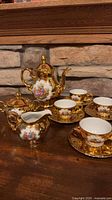 Full set on wooden surface showing teapot, sugar, creamer, three cup-saucer sets