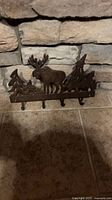 Front view of cast iron wall hook rack showing moose and pine trees design with four hooks