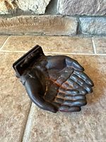 Top view of cast metal cupped hands sculpture showing patina and mounting bracket