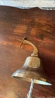 Side view of brass bell showing mounting bracket, bell shape and rope pull