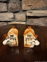 Front view of both ceramic outhouse shakers showing wording and attached figures