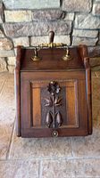 Front view showing carved floral panel, brass knob, brass/wood handle