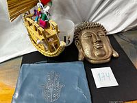 Overview showing all four items: Buddha head, reed boat, monogram candleholder, Hamsa pouch