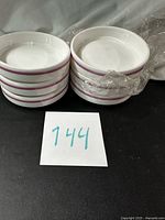 Two stacks of white ramekins with pink bands, plastic wrap on one stack