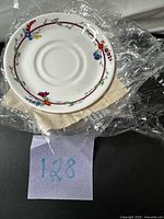 Top view of one saucer showing floral rim and maroon band, wrapped in factory plastic