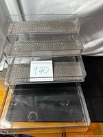 Four acrylic trays with fabric liners stacked over larger clear tray