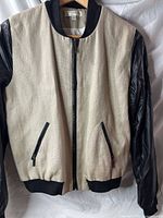 Front view of Kenar bomber jacket showing beige body, black sleeves, zipper closure and pockets