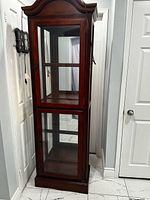 Full view of tall glass curio cabinet with cord visible