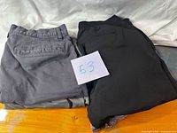 Stacked view of all four folded garments, showing dark gray chinos and black pants topmost