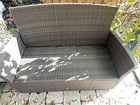 front angle of dark brown resin wicker loveseat bench showing armrests and seat platform
