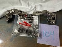 Two assembled polished nickel Richelieu concealed cabinet hinges and sealed bag of additional parts