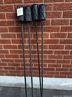 Four black metal torch stakes leaning against brick wall