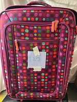 Front view of magenta polka dot softside suitcase with zip pockets