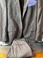 Full view of gray suit jacket on hanger with pants folded below